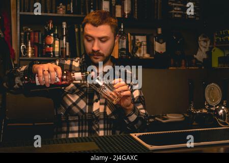 Bartender pouring pomegranate syrup from bottle into highball glass Stock Photo