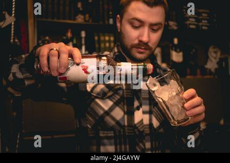 Bartender pouring grenadine syrup from bottle into glass with ice, preparing Tequila Sunrise cocktail Stock Photo