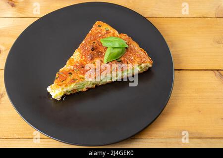 Courgette pie , triangle portion on a black irregular plate Stock Photo