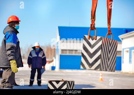 Working slinger passes exam on lifting loads. Real scene. Commission evaluates skill of slinger. Worker in helmet on street on winter day. Stock Photo