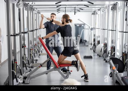 Man doing exercises on decompression simulators with the help of rehabilitation specialist Stock Photo