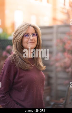 Mature white woman smiling in a happy attitude in the garden of her house. Stock Photo