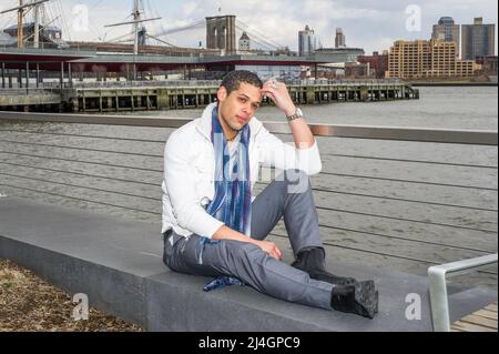 A young student is sitting by a river, scratching his head and into deeply thinking. Stock Photo