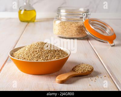 Raw white quinoa seeds in a bowl, wooden spoon and clip top glass jar on a white rustic table. Ingredient of gluten free dishes. Chenopodium quinoa. Stock Photo