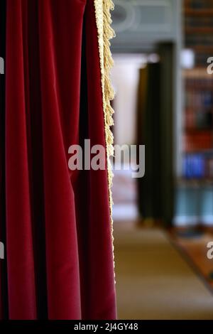 Red velvet curtain drawn open to an old library room Stock Photo