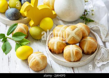 Happy Easter festive food concept. Homemade Easter traditional hot cross buns with raisin and natural colorful easter eggs on a rustic table. Stock Photo