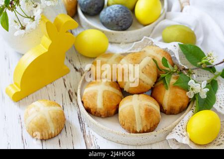Happy Easter festive food concept. Homemade Easter traditional hot cross buns with raisin and natural colorful easter eggs on a rustic table. Stock Photo