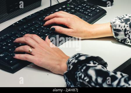 closeup caucasian hands of female worker with black nails, typing on the computer keyboard inside the office. Stock Photo