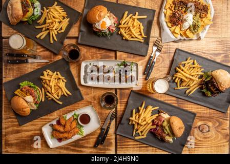 Set of fast food dishes and assorted beef burgers, meatballs with cream cheese, phyto eggs, nachos with guacamole, chicken fingers on wooden table Stock Photo