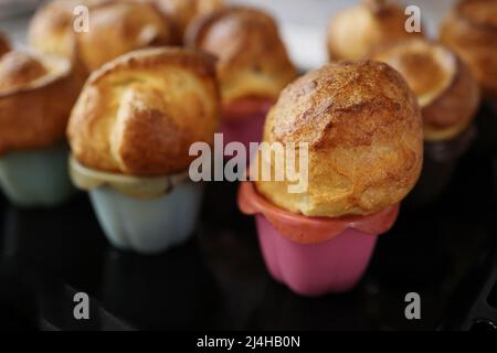 Homemade popover, which is a lush, airy and egg hollow roll, fresh from the oven. Yorkshire pudding freshly baked in silicone blue and pink baking dis Stock Photo