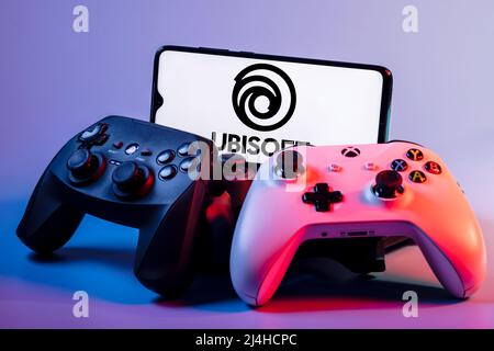 Ubisoft is French video game company. Smartphone with Ubisoft logo on screen on pile of gamepads. Stock Photo