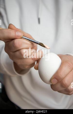 Paint brush in woman's hand and clean white chicken egg. A woman prepares to start painting eggs in Easter holidays in April. DIY Easter preparation c Stock Photo