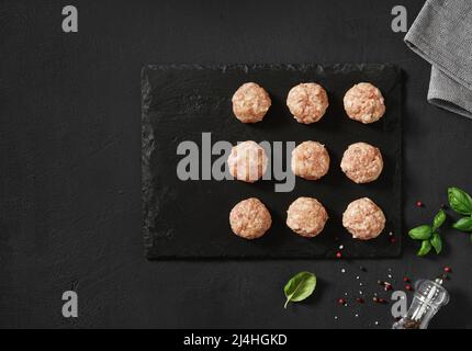 Raw meatballs with basil. Black background. Top view Stock Photo