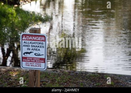 A sign by a river in Orlando, Florida, USA, warns of alligators and snakes in the area. Stock Photo
