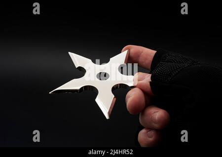 Martial arts skill and traditional Japanese weapon concept with hand in fingerless ninja glove trowing metal star shaped shuriken isolated on black ba Stock Photo