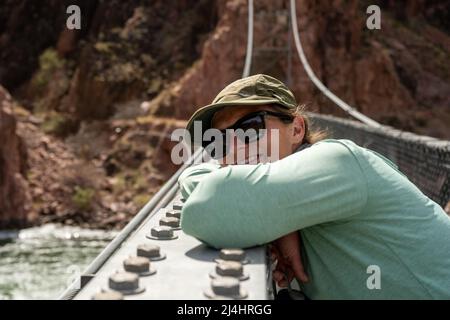 Woman In Sunglasses Leaning On The Railing Of The Silver Bridge in the Grand Canyon Stock Photo