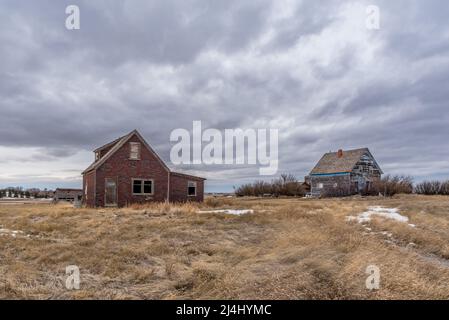 A moody sky over two old, abandoned homes on the prairies of Saskatchewan Stock Photo