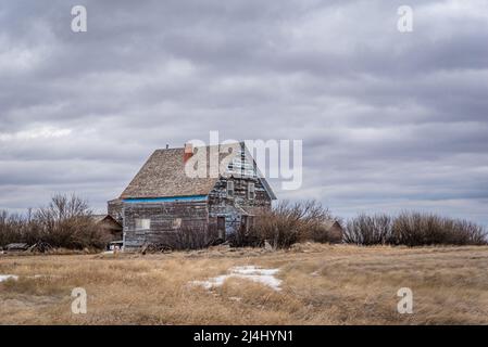 A moody sky over an old, abandoned blue home on the prairies of Saskatchewan Stock Photo