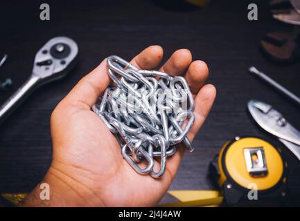 A metal chain on the mechanic hand with a mechanic tools on wooden background Stock Photo
