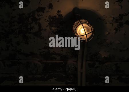 Old industrial light with tungsten lamp mounted on grunge wall glowing in dark, close-up photo with selective focus Stock Photo