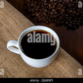 White cup of coffee with coffee beans on wooden background Stock Photo