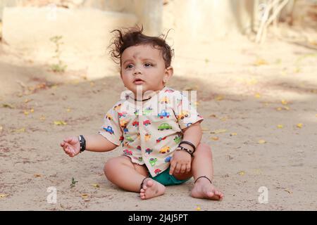 close-up of portrait photo of A small newborn cute Hindu baby sitting on the ground outside, india Stock Photo