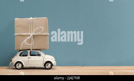 Retro white toy car delivering gift box atop on blue background Stock Photo