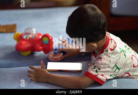 a toddler baby boy engaged in watching and exploring mobile phone.Screen time addiction concept image. Stock Photo
