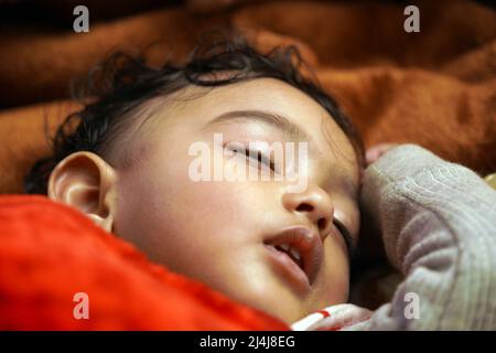 a one year baby sleeping with mouth partially open with hand by the side of the head with selective focus on left eye lash. Stock Photo