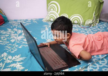 a toddler baby boy engaged in watching and exploring laptop.Screen time addiction concept image. Stock Photo