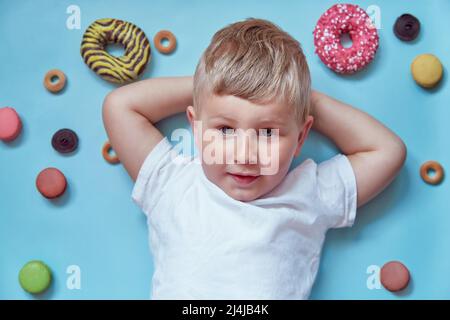 Cute smiling child on donuts and french macarons on blue background. National Donut Day concept. Happy childhood concept. Mock up white T-shirt.