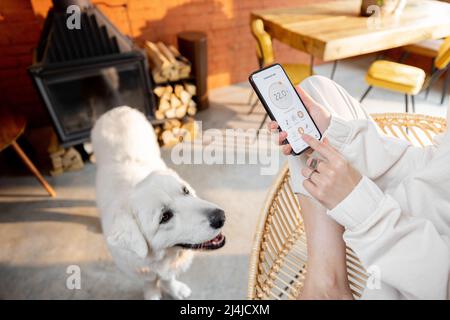 Woman using smart phone with running smart home app at home with her dog Stock Photo
