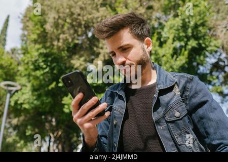 Side view portrait of a sad man in a lonely city park using a smart phone. Man reading a message or checking phone messages or watching video Stock Photo
