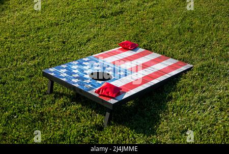 Two red bean bags on a cornhole game that is painted as an American flag on a green grass field. Stock Photo