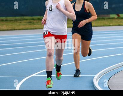 Front view of two high school girls running a race on a blue track outdoor. Stock Photo
