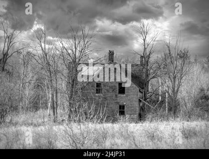 An old black and white abandoned haunted spooky looking farmhouse in winter on a farm yard in rural Canada Stock Photo