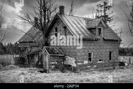 An old black and white abandoned haunted spooky looking farmhouse in winter on a farm yard in rural Canada Stock Photo