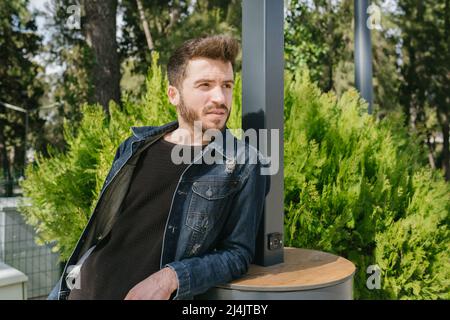 Leaning on the back, young man leans back on public charging station, tired of the heat and looking for a place to rest Stock Photo