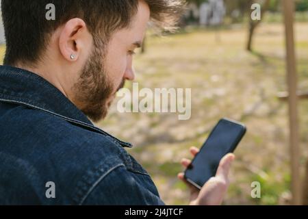 Young man looking at phone display, man in denim jacket looking at black screen, online shopping and internet surfing Stock Photo