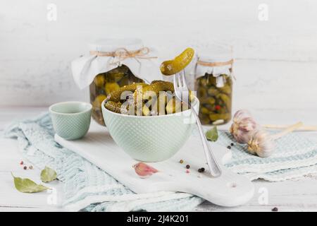 Gherkins, pickled cucumber on a fork, bowl of marinated vegetables on a white wooden background Stock Photo