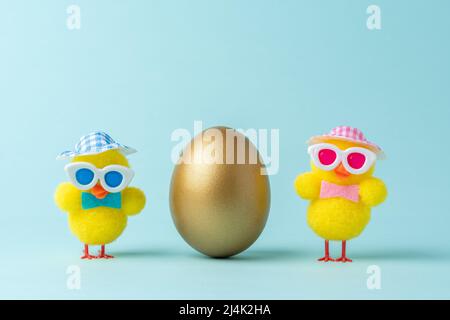 Creative composition with gold Easter egg and chickens on blue background. Minimal Easter background. Spring holidays concept. Stock Photo