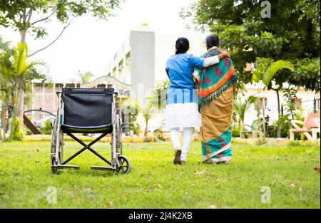 focus on armchair, Nurse taking walk by supporting senior old woman from wheelchair - concept rehabilitation, caretaker and medicare treatment Stock Photo