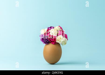 Spring flowers in cracked eggshell against pastel blue background. Easter minimal concept. Creative Happy Easter or spring layout. Stock Photo