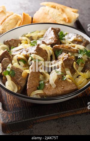 delicious veal liver pieces stir fried and stewed with onion rings closeup in the bowl on the table. Vertical Stock Photo