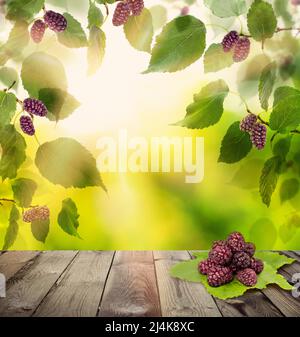 Mulberry fruits on rustic wooden board against abstract greenery foliage background Stock Photo
