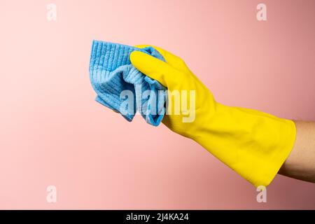 a hand with a yellow rubber glove holds a cleaning sponge with a ...