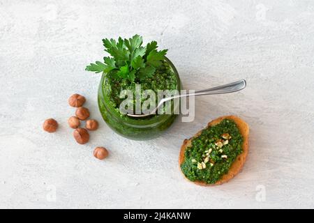 Fresh homemade parsley pesto with hazelnuts in glass jar and bread on light gray background. delicious vegan food Stock Photo