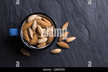 Mug with garden and mountain almonds in shell on black slate background, top view, free space Stock Photo