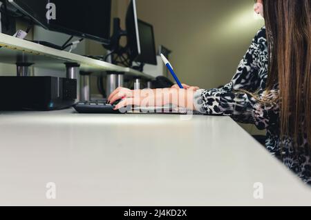 young female employee worker in office sitting using computer and writing notes from her clients, software programming office worker, copy space Stock Photo