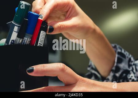 closeup caucasian young female hands inside an office taking colored markers from the pen holder, copy space Stock Photo